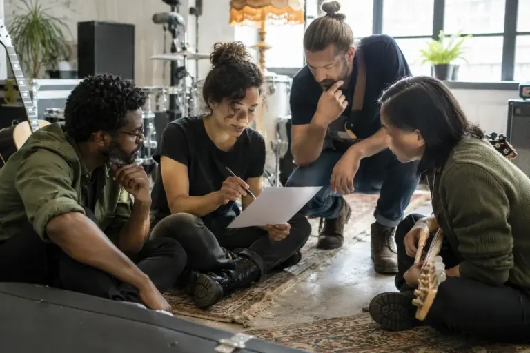 A small band discussing a blank setlist sheet beside instruments before rehearsal.