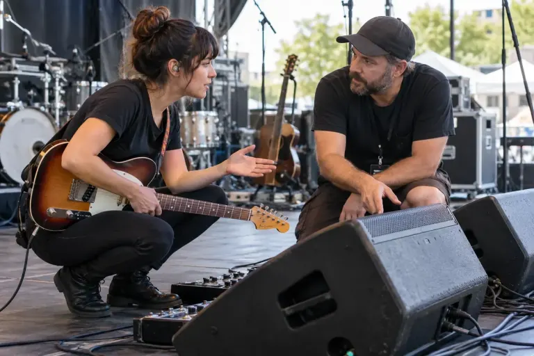 A musician talking with a sound engineer beside stage monitor speakers before a small performance.